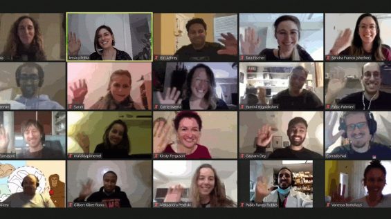 A group of diverse individuals participating in a video call. Each person is in a separate video box, smiling and waving at the camera. The background of each video varies, indicating they are each in different locations.
