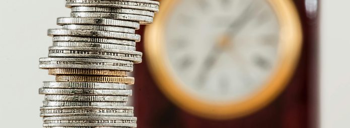A stack of coins with an out of focus clock in the background