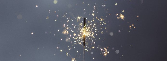 A hand holding a lit sparkler against a dark background