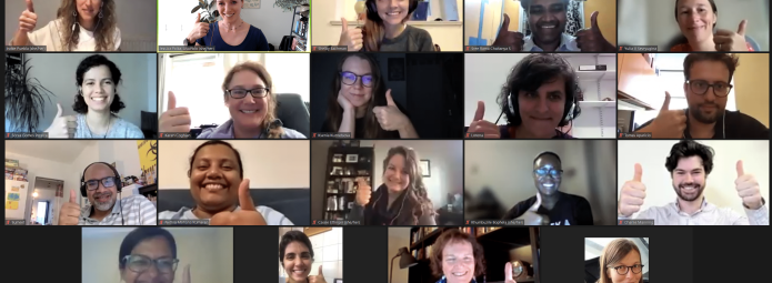 A group of sixteen people are in a virtual meeting, each giving a thumbs-up gesture. They appear to be smiling and happy, and the diverse group is displayed in a grid format typical of video calls.