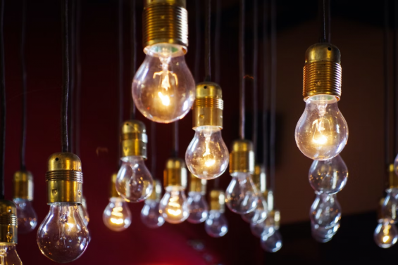 A cluster of hanging light bulbs with brass fixtures, some illuminated and others off, against a dark red background, creating a warm, ambient atmosphere.